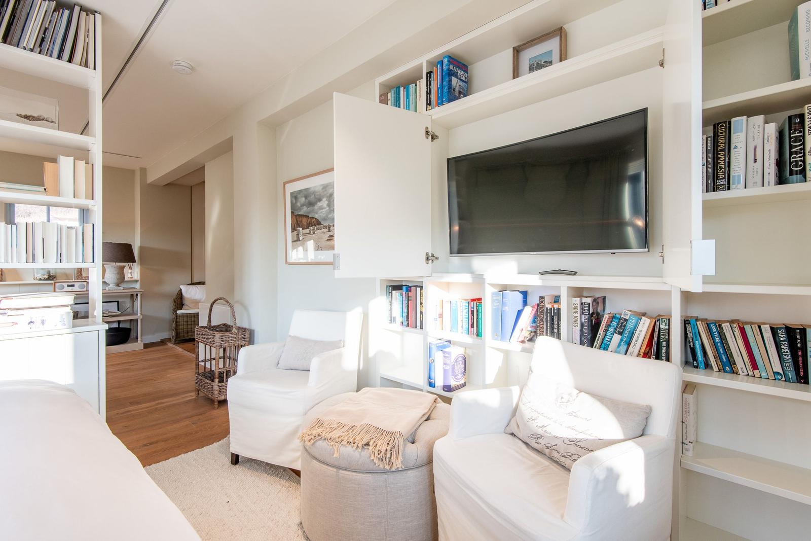 Wohnbereich mit Bücherregalen, TV und weißen Sesseln.