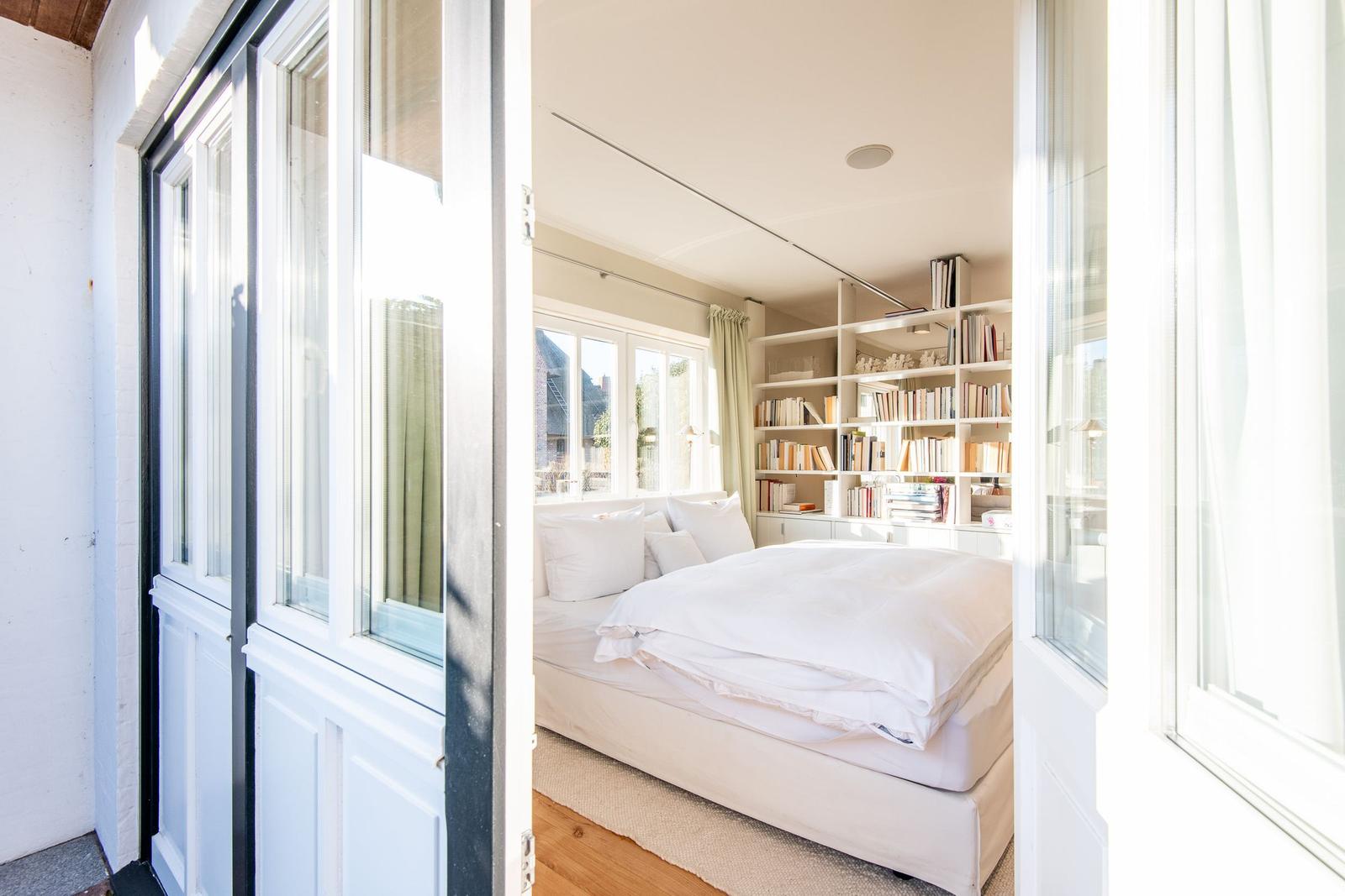 Schlafzimmer mit weißem Bett und Bücherregal an der Wand.