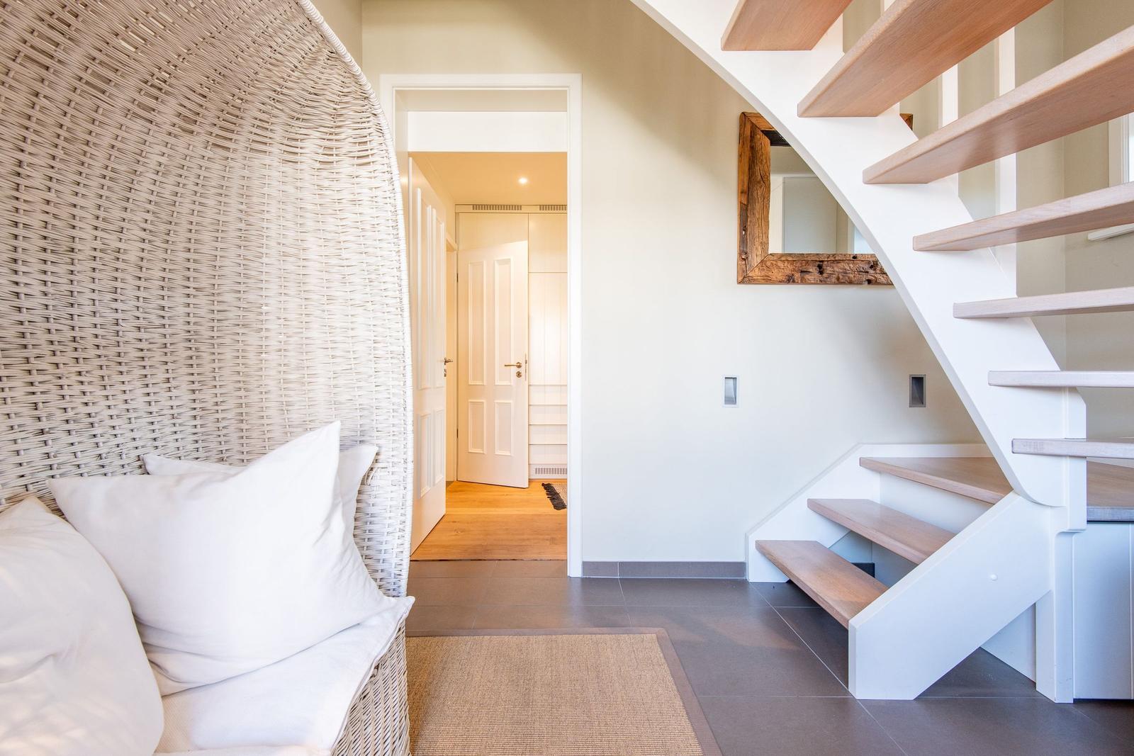 Wohnbereich mit Rattan-Sessel, Treppe und Spiegel an der Wand.