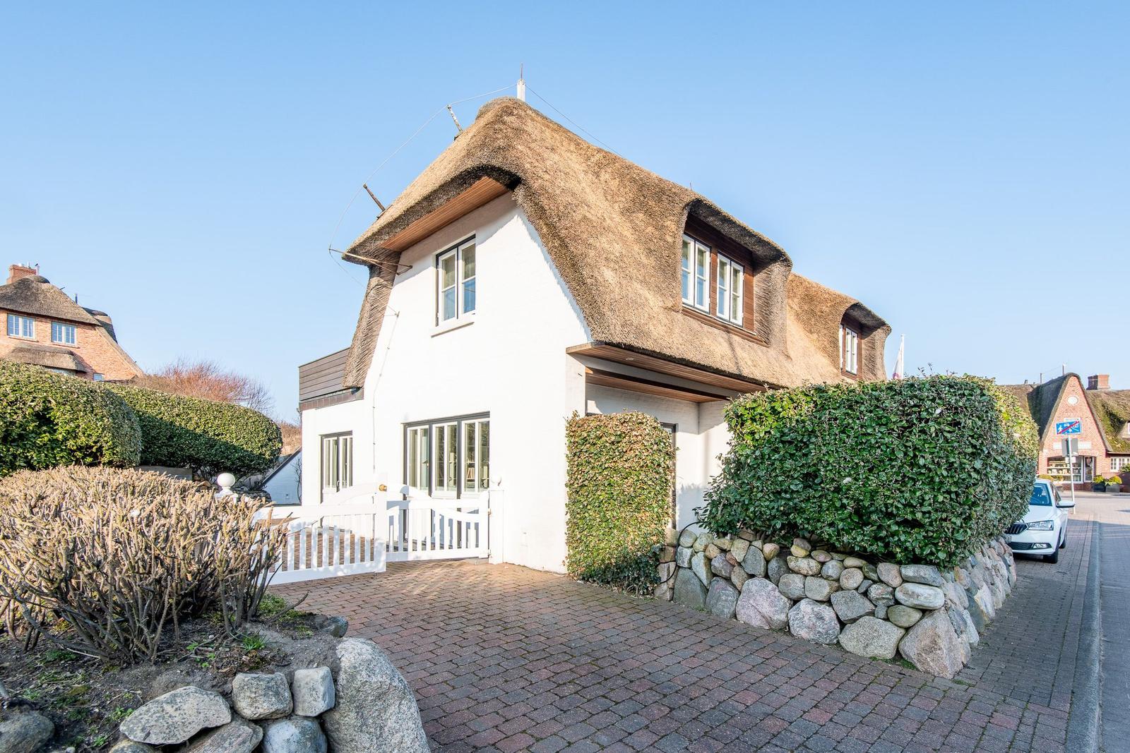 Wohnhaus mit Strohdach, weißen Wänden und gepflastertem Hof.