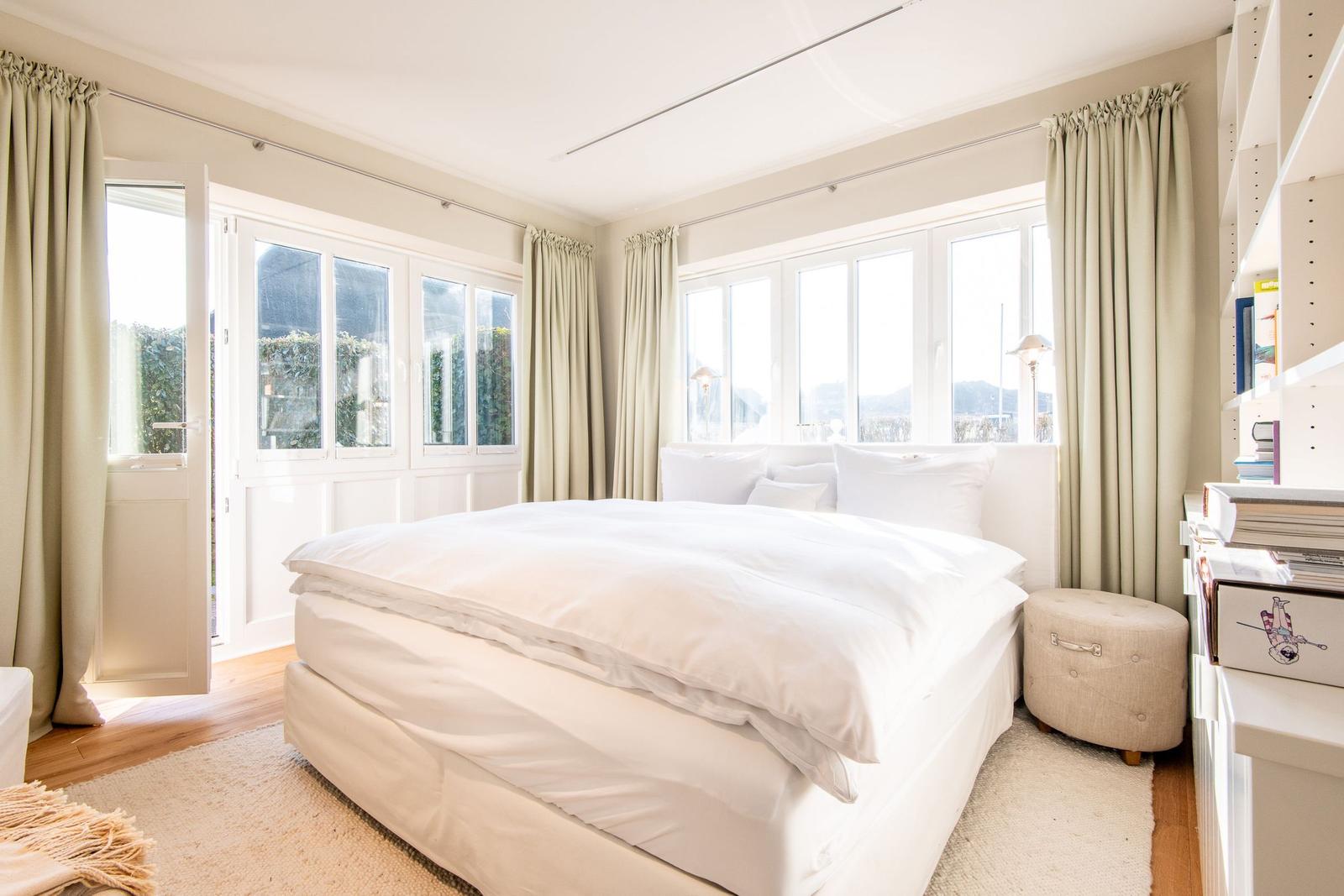 Schlafzimmer mit weißem Bett, großen Fenstern und Holzboden.