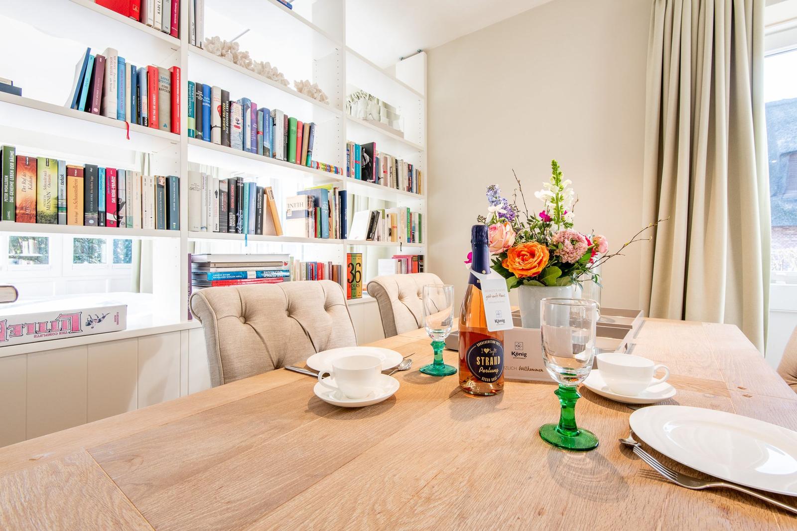 Esstisch mit Stühlen, Bücherregal und Blumenvase.