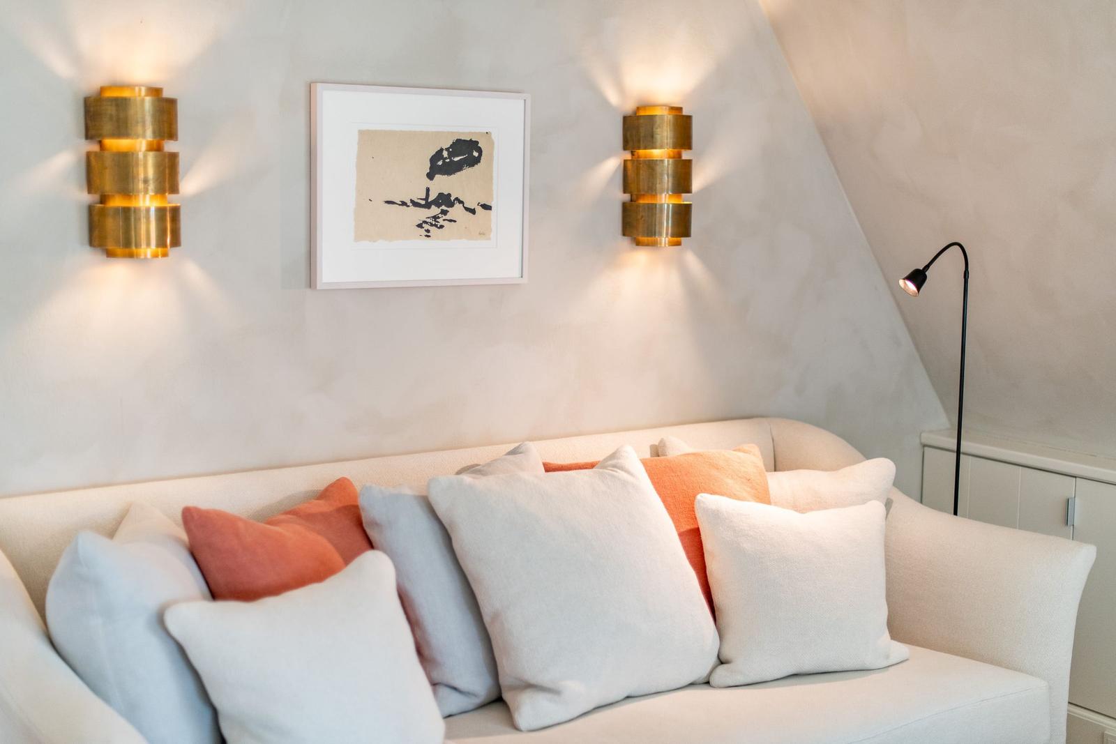 Ein Sofa mit Kissen unter zwei Wandlampen und einem Bild an der Wand.