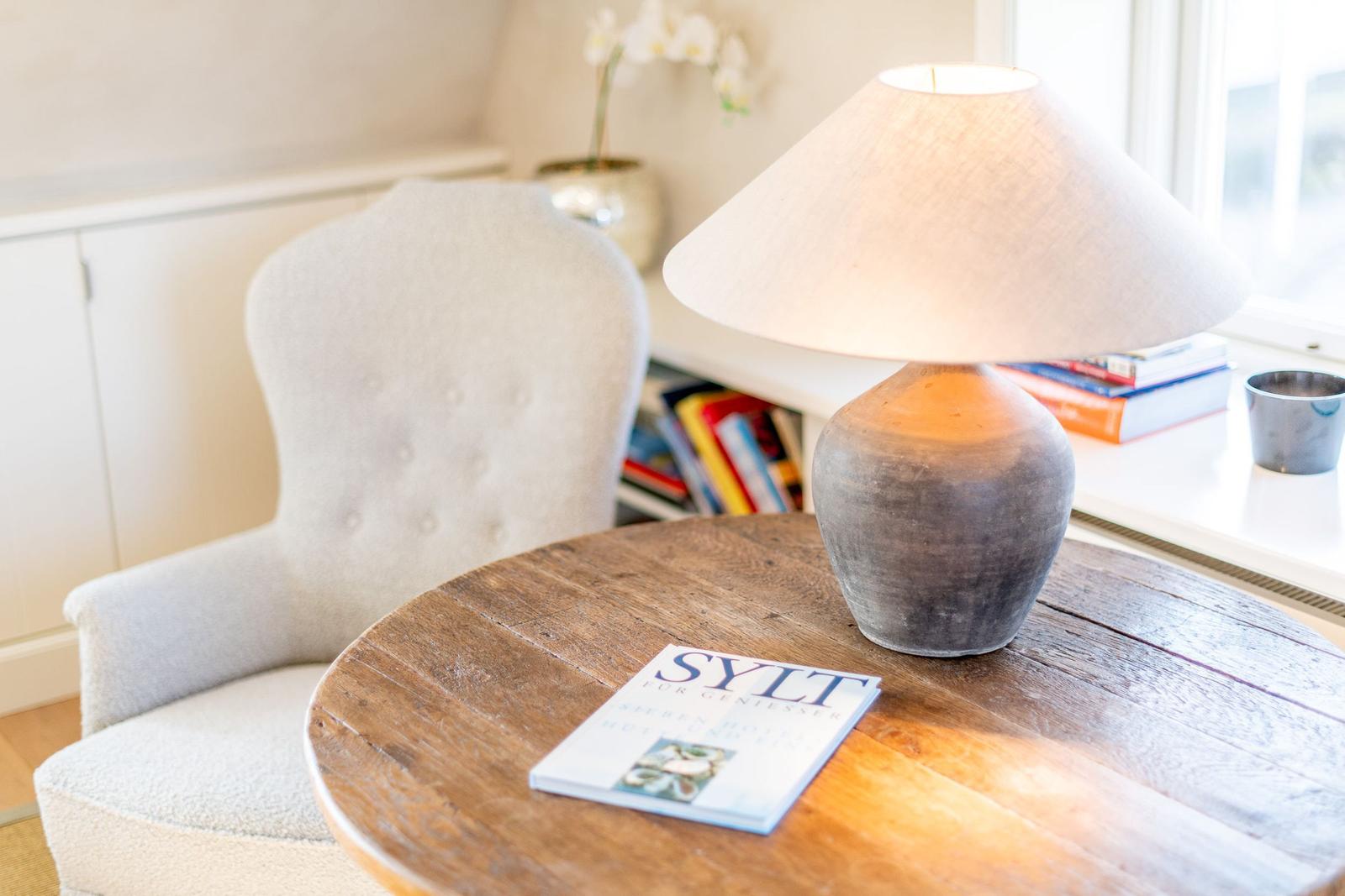 Runder Tisch mit Lampe und Buch neben einem Sessel.