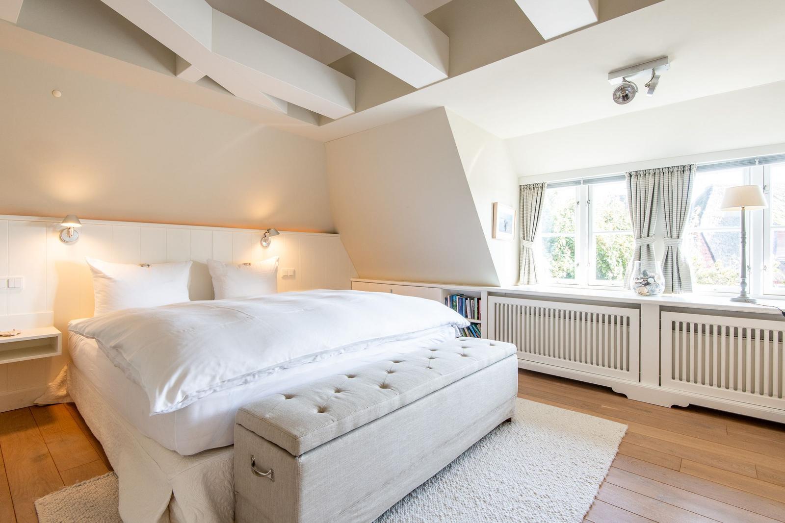 Schlafzimmer mit weißem Bett, Holzboden und großem Fenster.