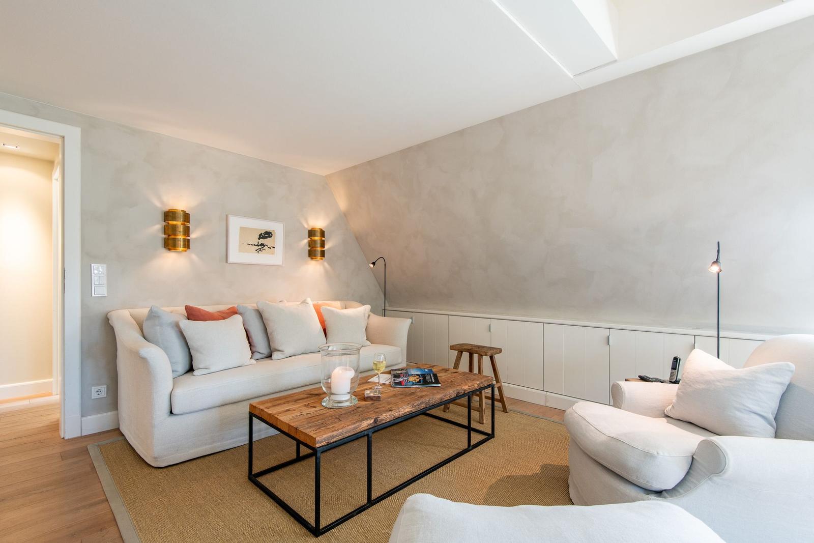 Wohnzimmer mit Sofa, Sessel und Holztisch unter Dachschrägen.