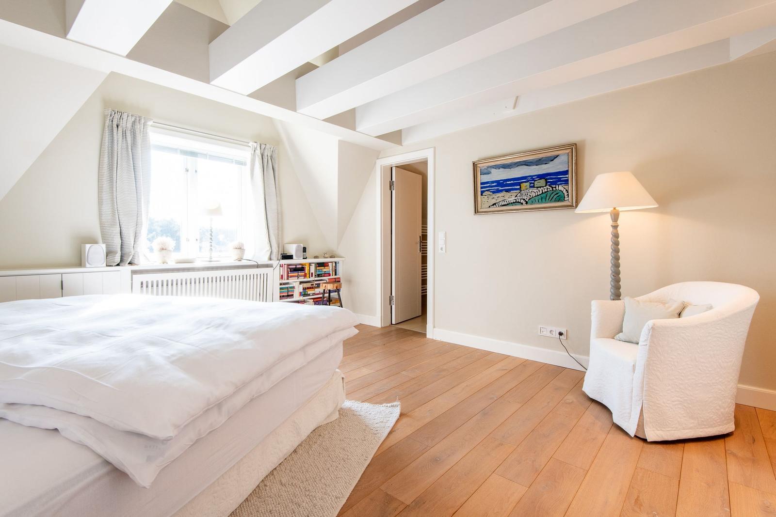 Schlafzimmer mit Dachschräge, weißem Bett und Holzboden.