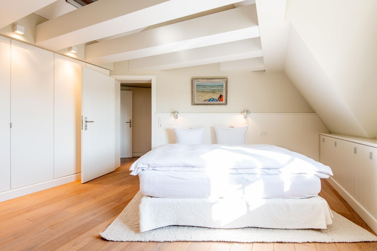 Schlafzimmer mit Dachschräge, weißem Bett und Holzboden.