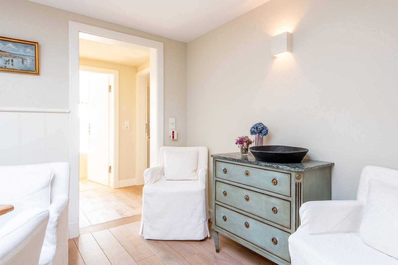 Ein Raum mit zwei weißen Sesseln, einem blauen Schrank und einer Wandlampe.