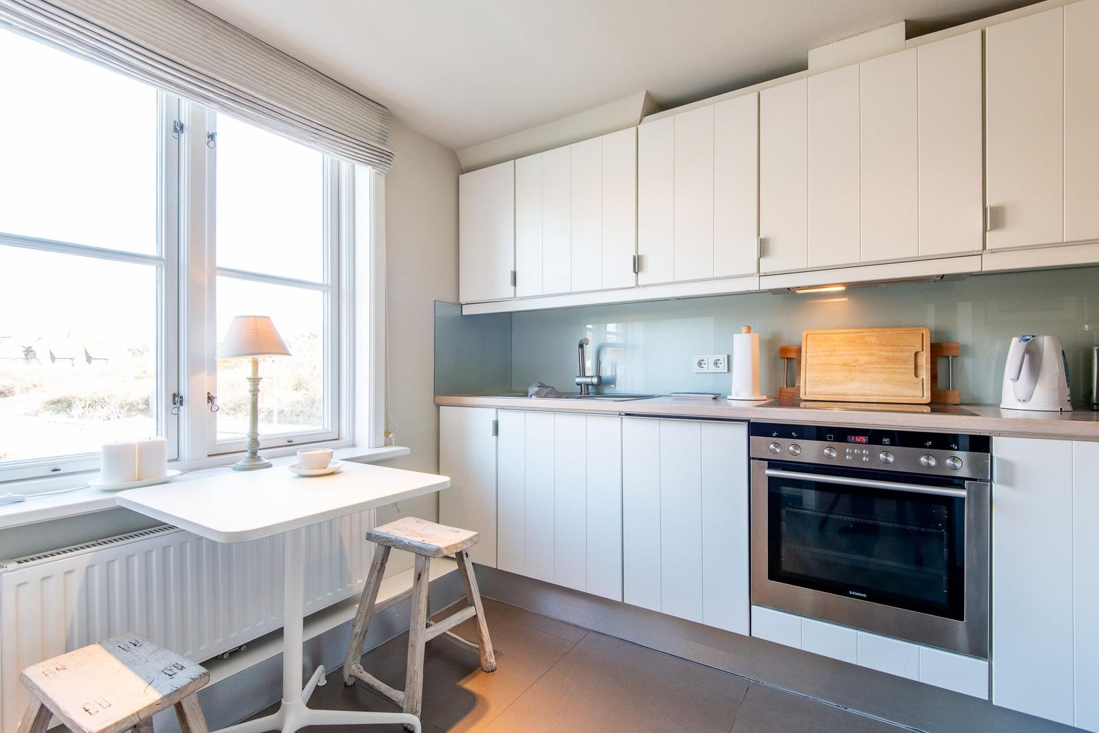 Küche mit weißen Schränken, Edelstahlherd und kleinem Tisch mit Hocker.