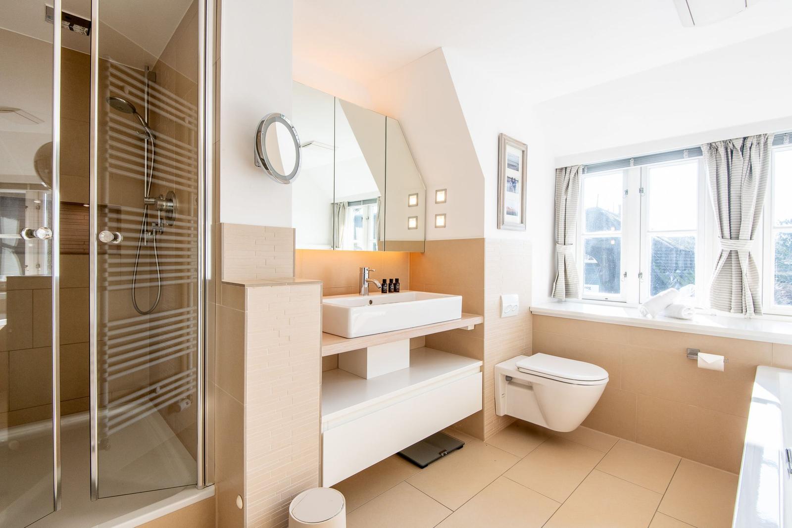 Badezimmer mit Dusche, Waschbecken und Toilette. Fenster mit Vorhängen.