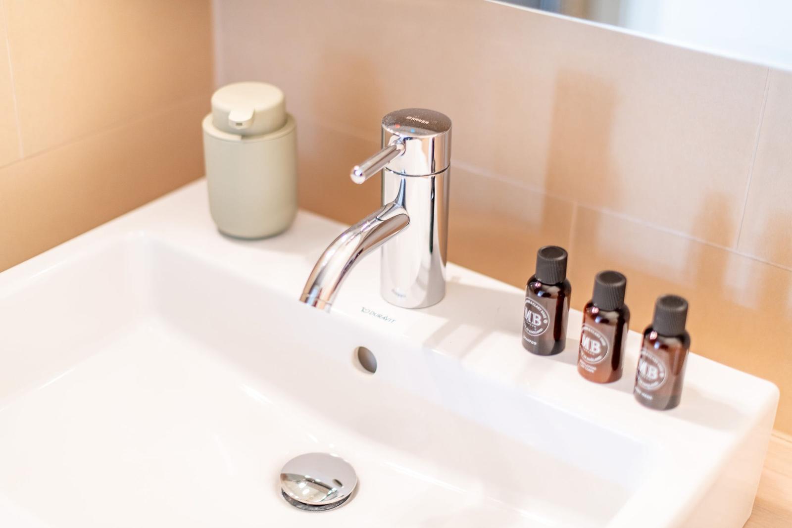 Waschbecken mit Wasserhahn und drei kleinen Fläschchen.