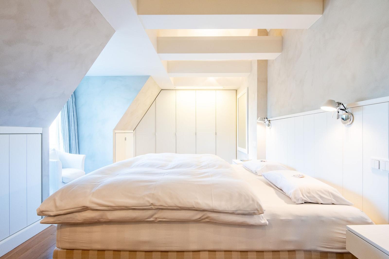 Schlafzimmer mit Doppelbett, weißen Wänden und Holzboden. Dachschräge und integrierte Schränke.