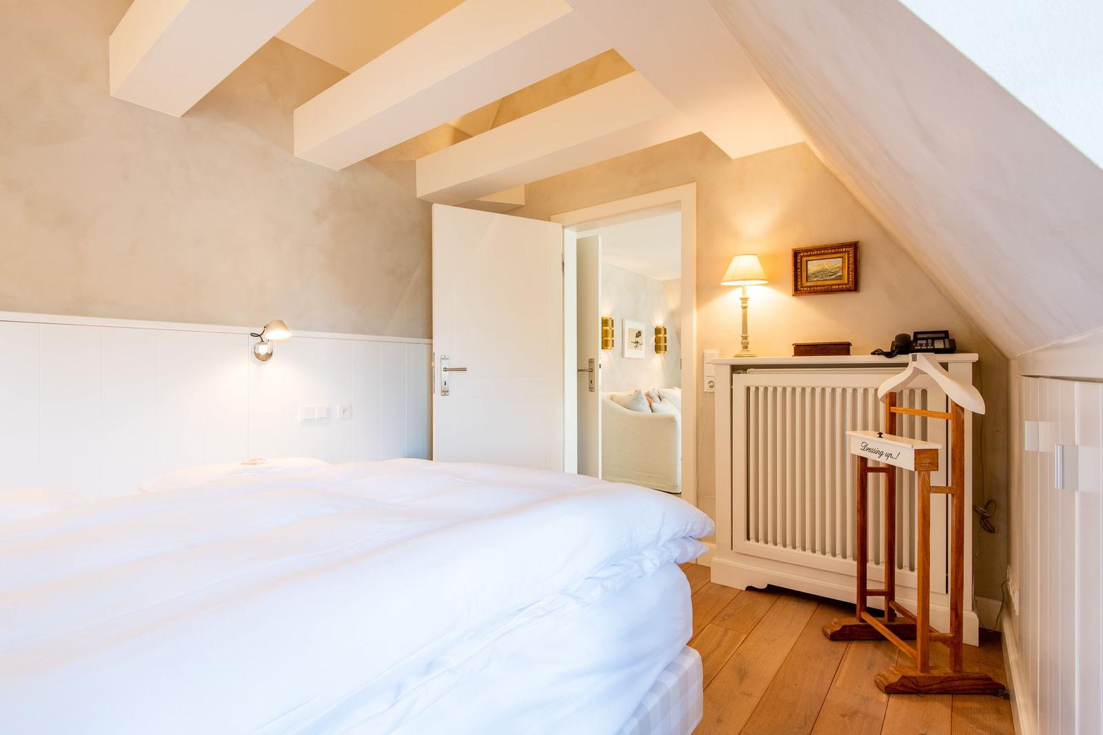 Schlafzimmer mit Dachschräge, Bett, Kleiderständer und Tür zum Wohnbereich.