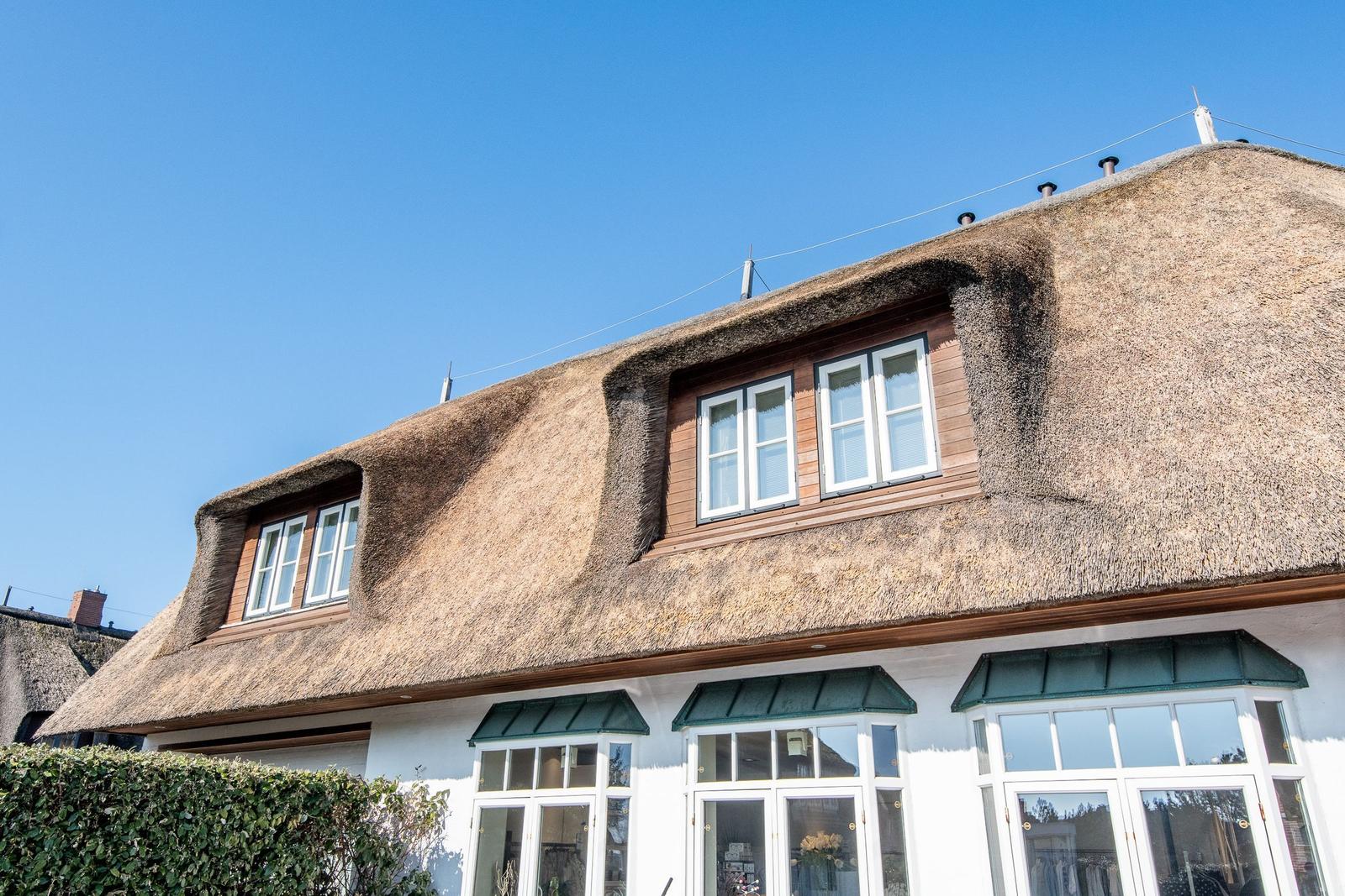 Haus mit Strohdach und weißen Fenstern unter blauem Himmel