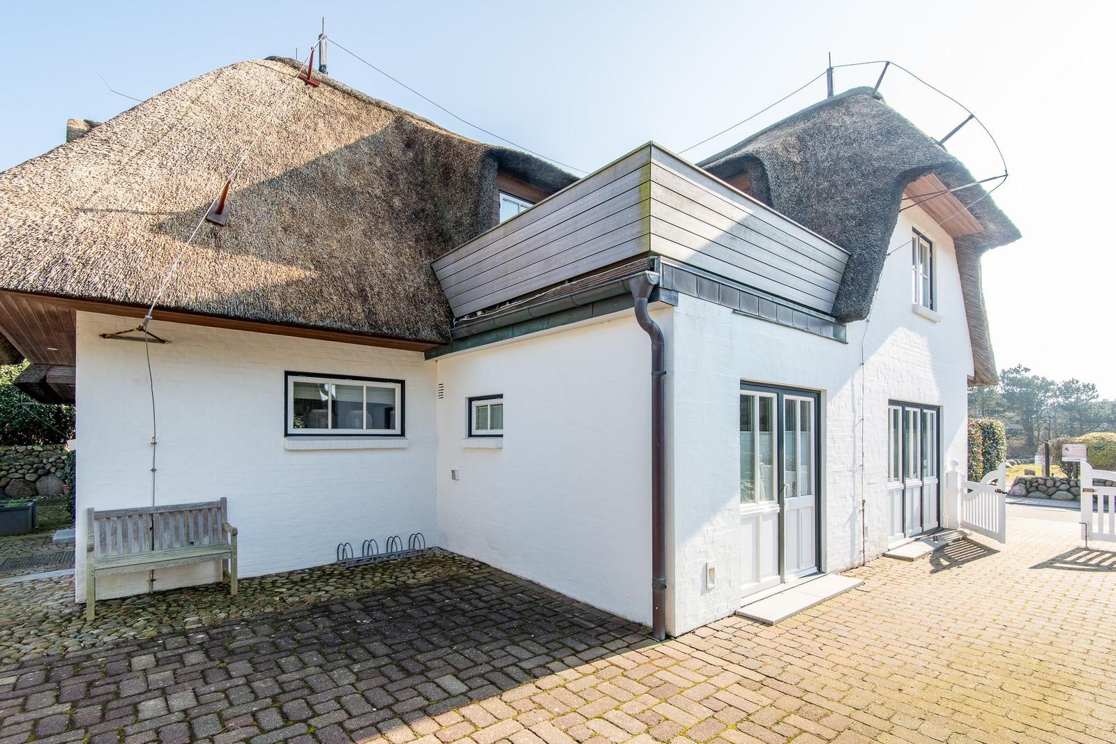 Wohnhaus mit Strohdach, weißer Fassade und Steinpflasterhof.