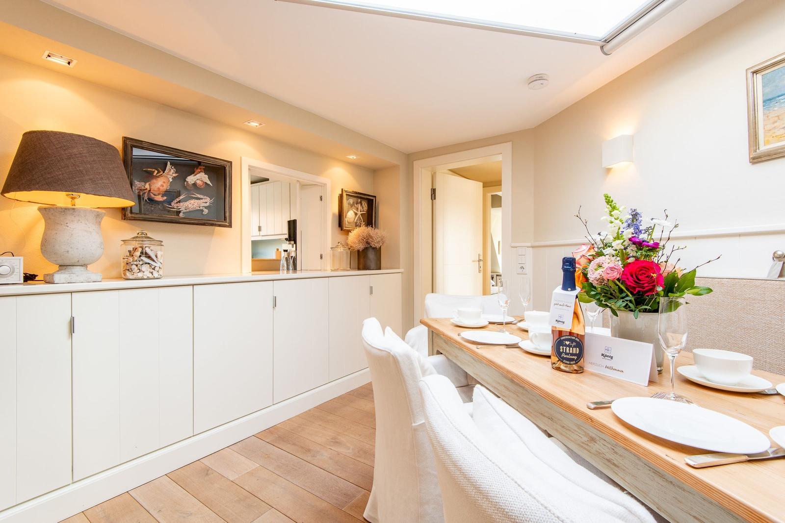 Esszimmer mit Holztisch, weißen Stühlen und dekorativen Elementen an der Wand.