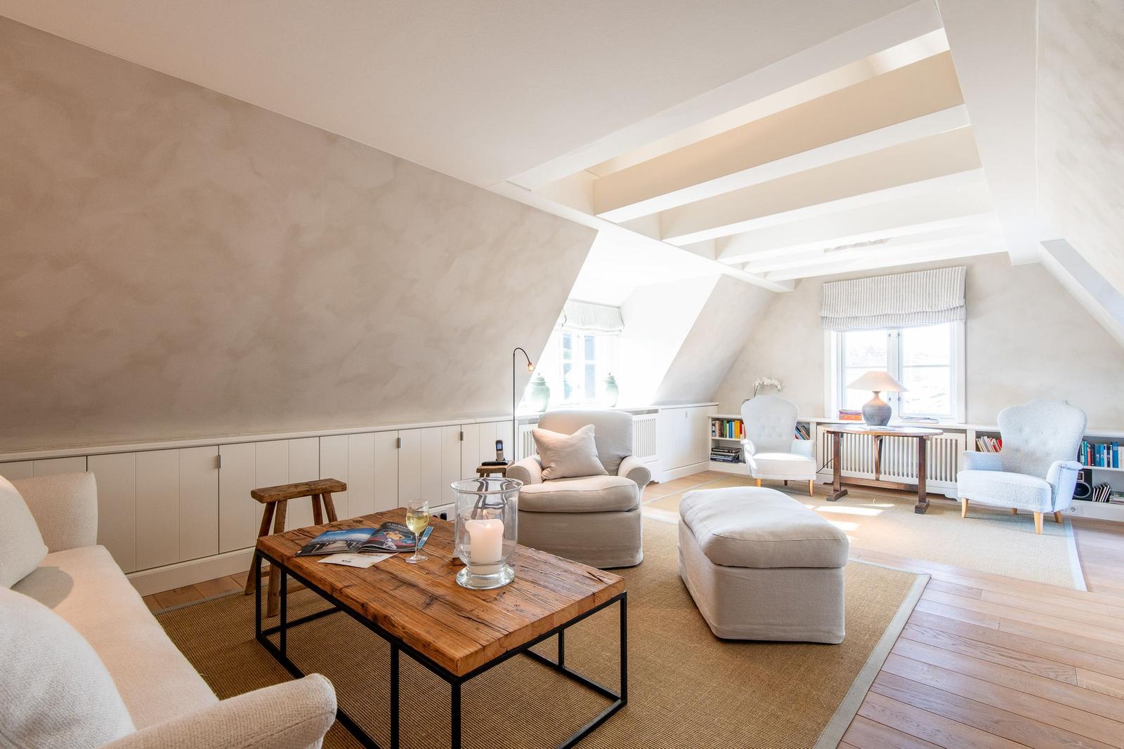 Dachgeschosswohnung mit Sitzgruppe, Tisch und Fenstern.