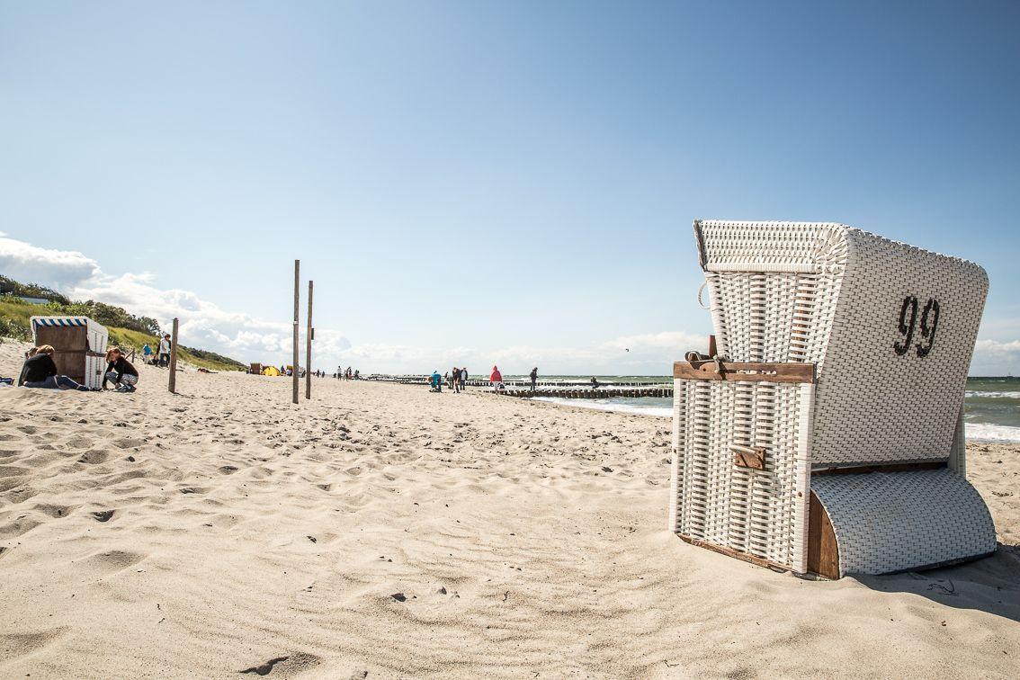 Strand mit weißen Strandkörben und Menschen in der Ferne.