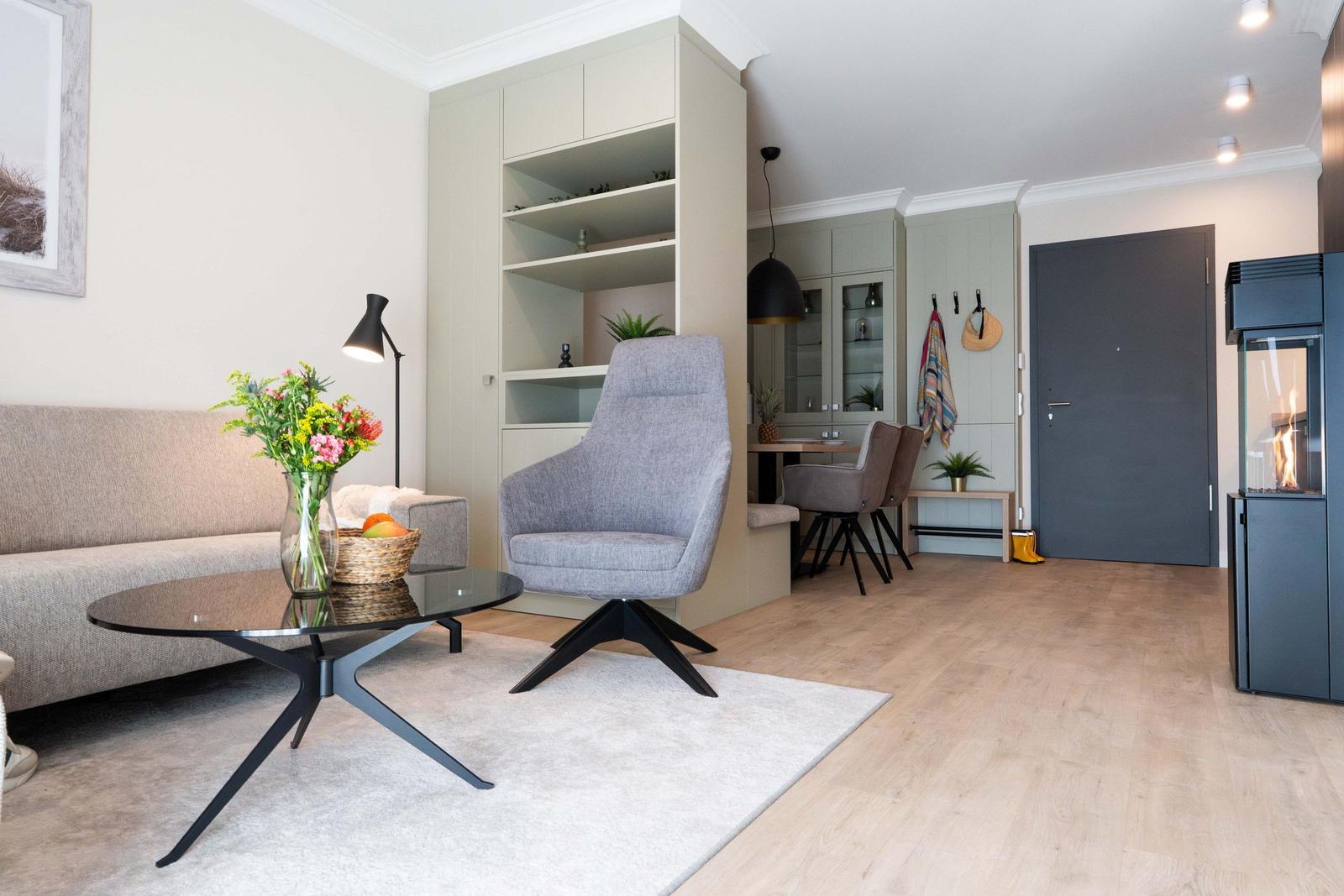 Wohnbereich mit Sofa, Sessel und Esstisch. Kaminofen und Holzfußboden sichtbar.
