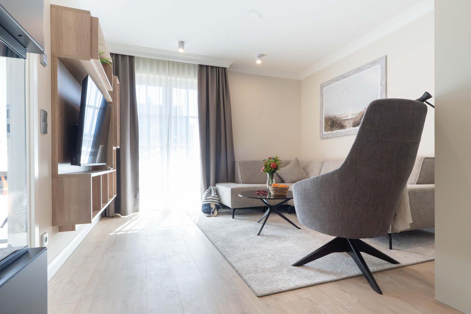 Wohnzimmer mit Sofa, Sessel und Fernseher an Wand