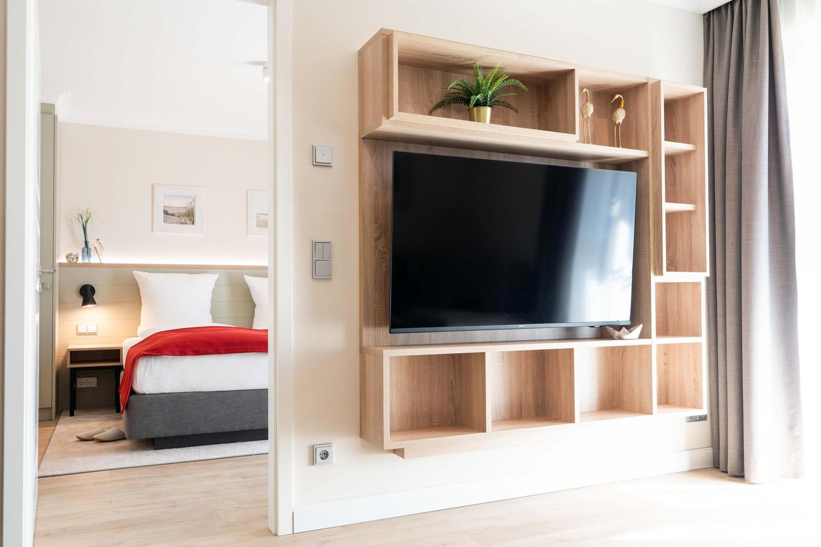 Wohnbereich mit TV-Möbel und Blick in Schlafzimmer mit Bett und Nachttisch.