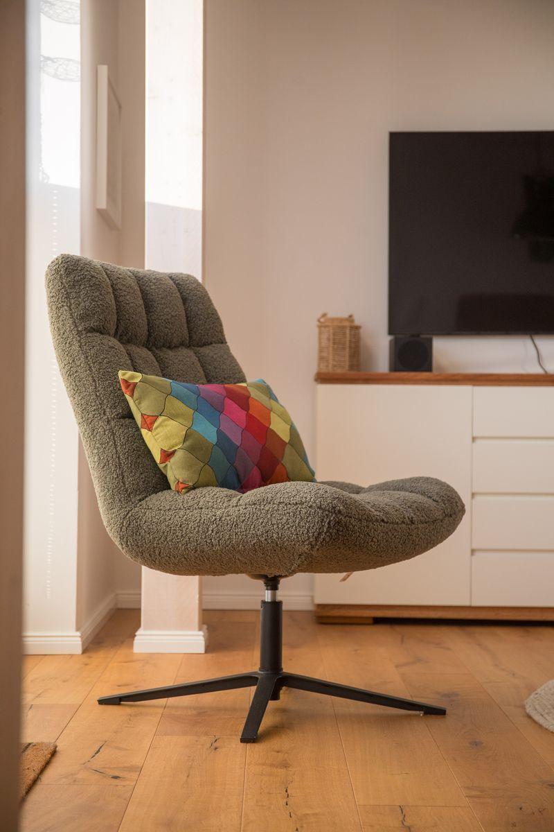 Ein grauer Sessel mit buntem Kissen steht vor einem Fernseher.