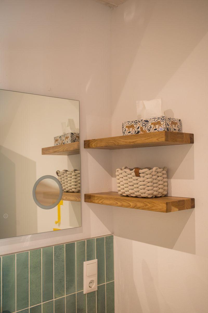 Badezimmer mit Holzregalen, Spiegel und grünen Fliesen.