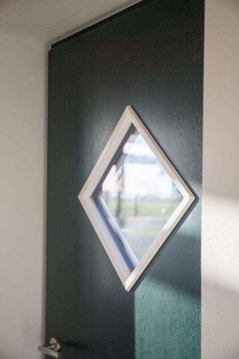 Schwarze Tür mit weiß gerahmtem Diamantfenster. Blick auf Außenbereich.