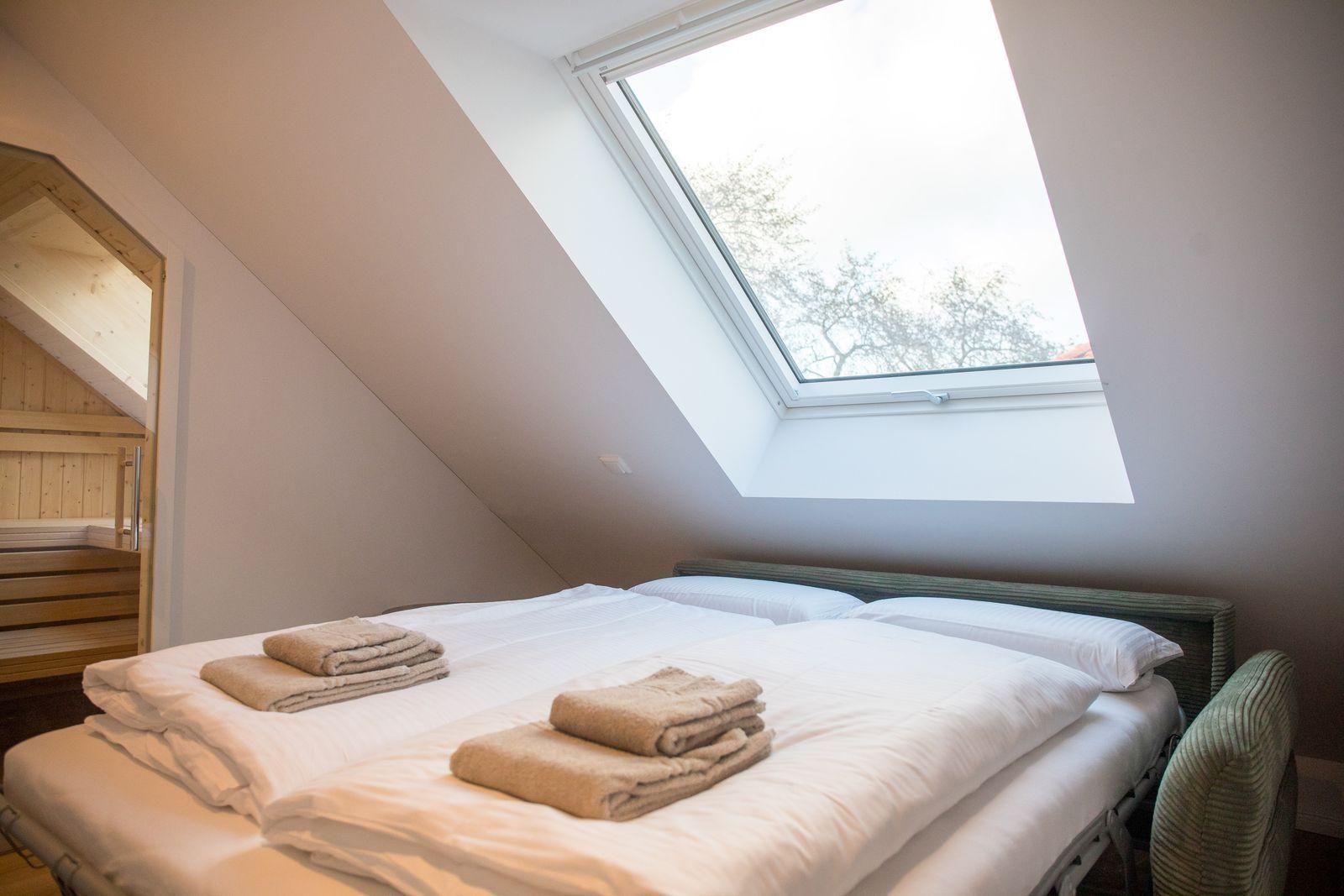 Schlafzimmer mit Dachfenster und Blick auf Bäume. Bett mit weißen Laken und gefalteten Handtüchern.