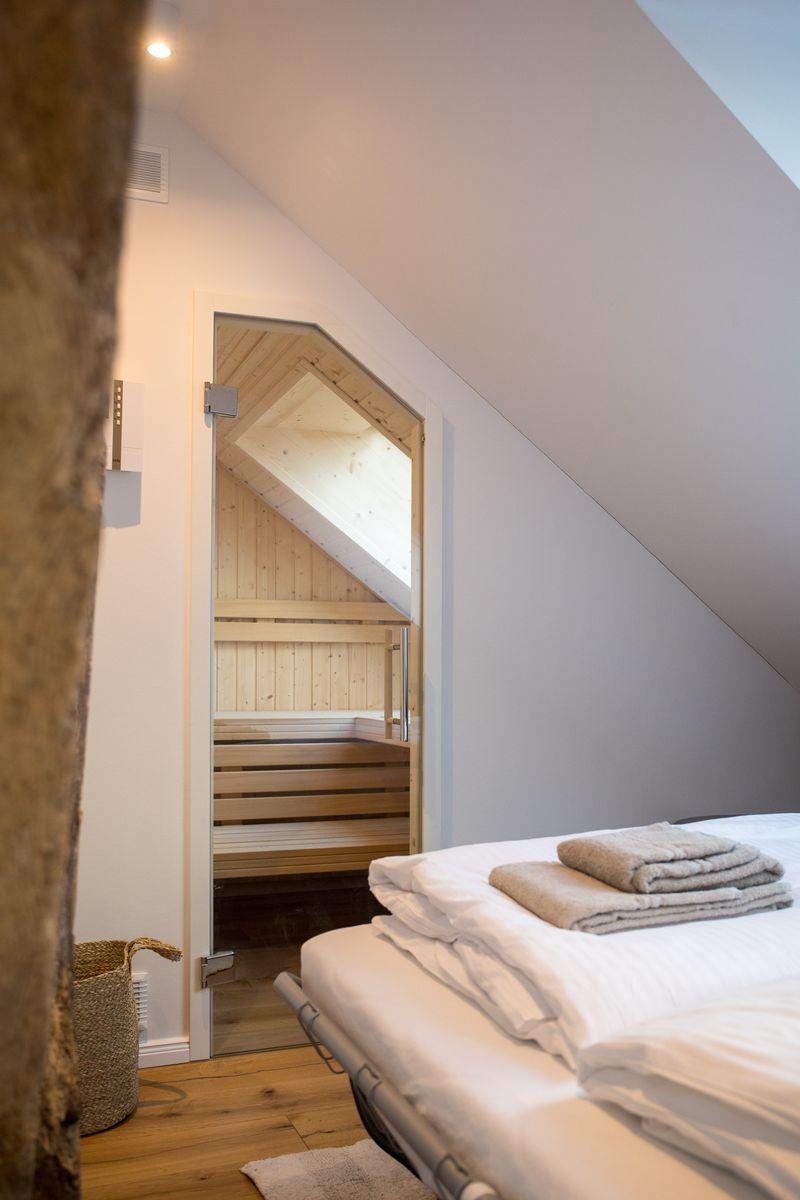 Schlafzimmer mit Blick in eine Holzsauna mit Sitzbänken.