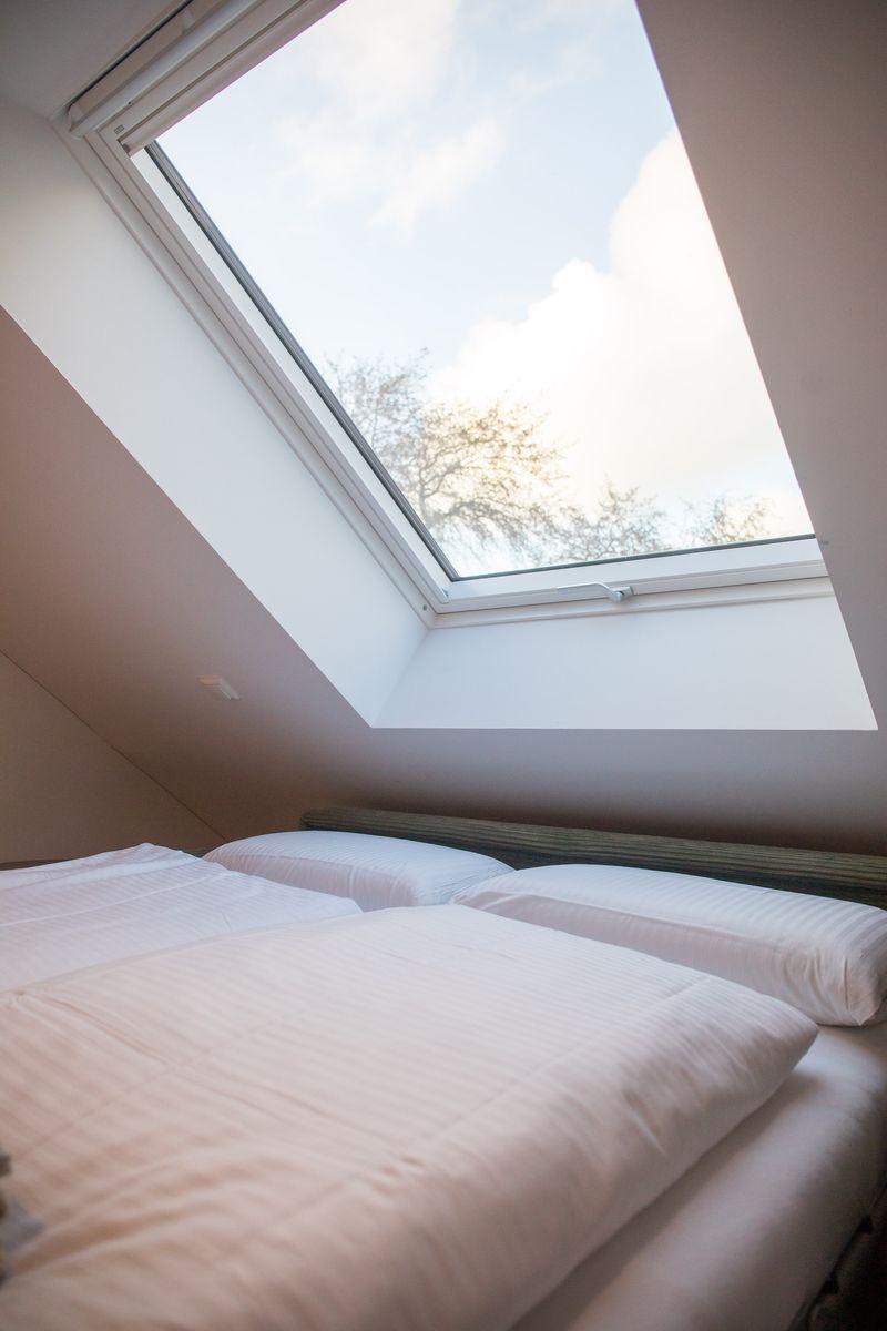 Schlafzimmer mit Dachschrägen und Dachfenster, Blick auf Bäume.