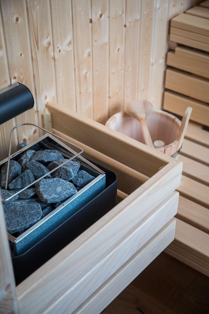 Sauna mit Steinmulde, Holzbank und Eimer mit Löffel.