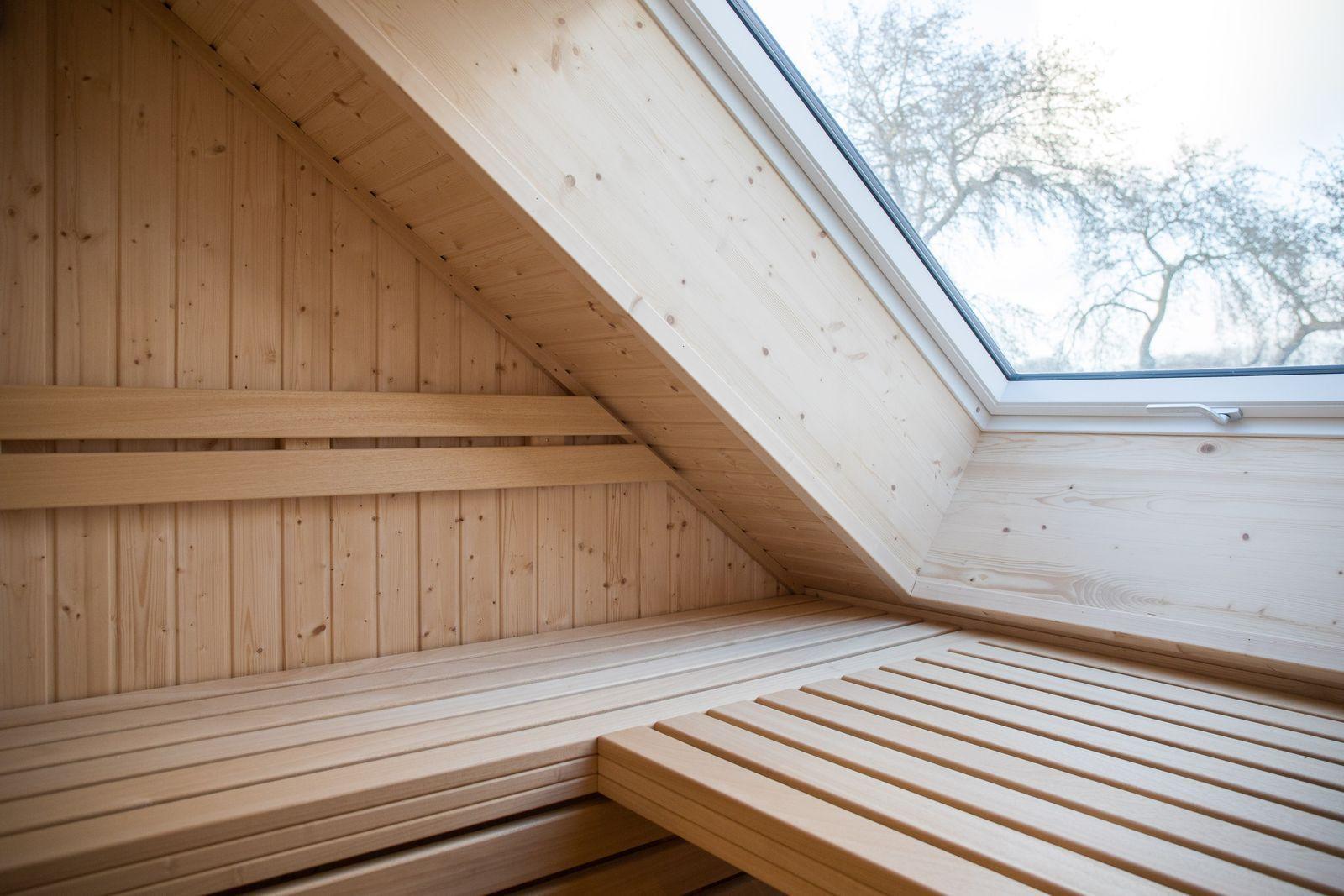 Holzsauna mit Dachschrägen und Fensterblick auf Bäume