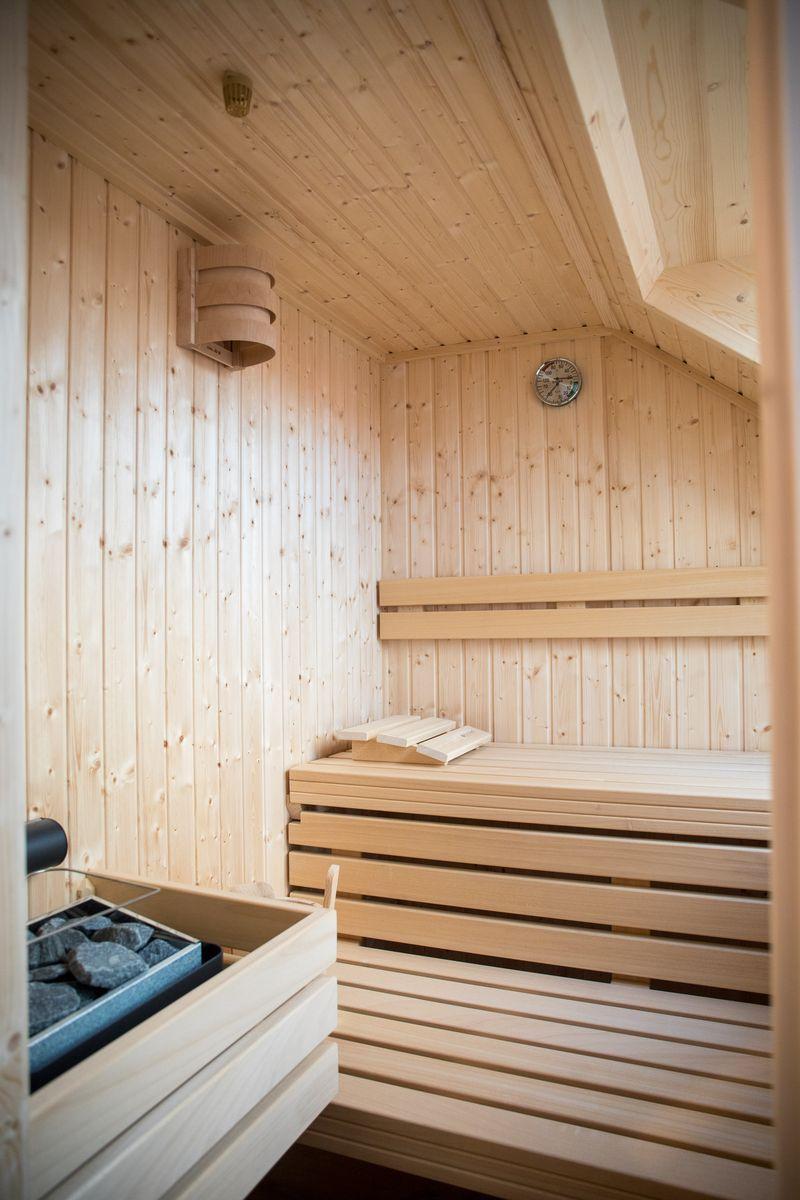 Sauna mit Holzbank, Wanduhr und Steinkasten.