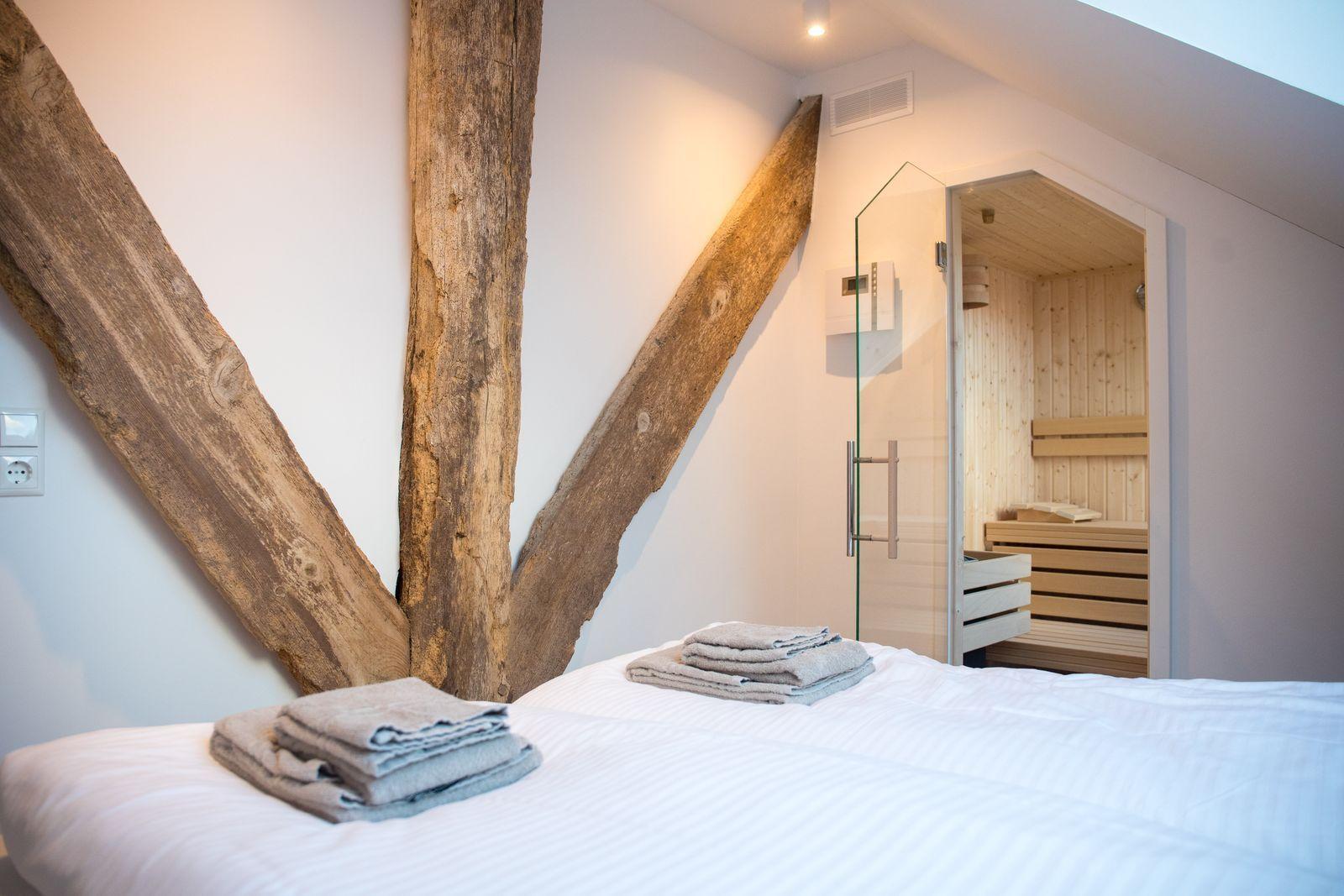 Schlafzimmer mit Bett, Holzpfosten und Sauna im Hintergrund.