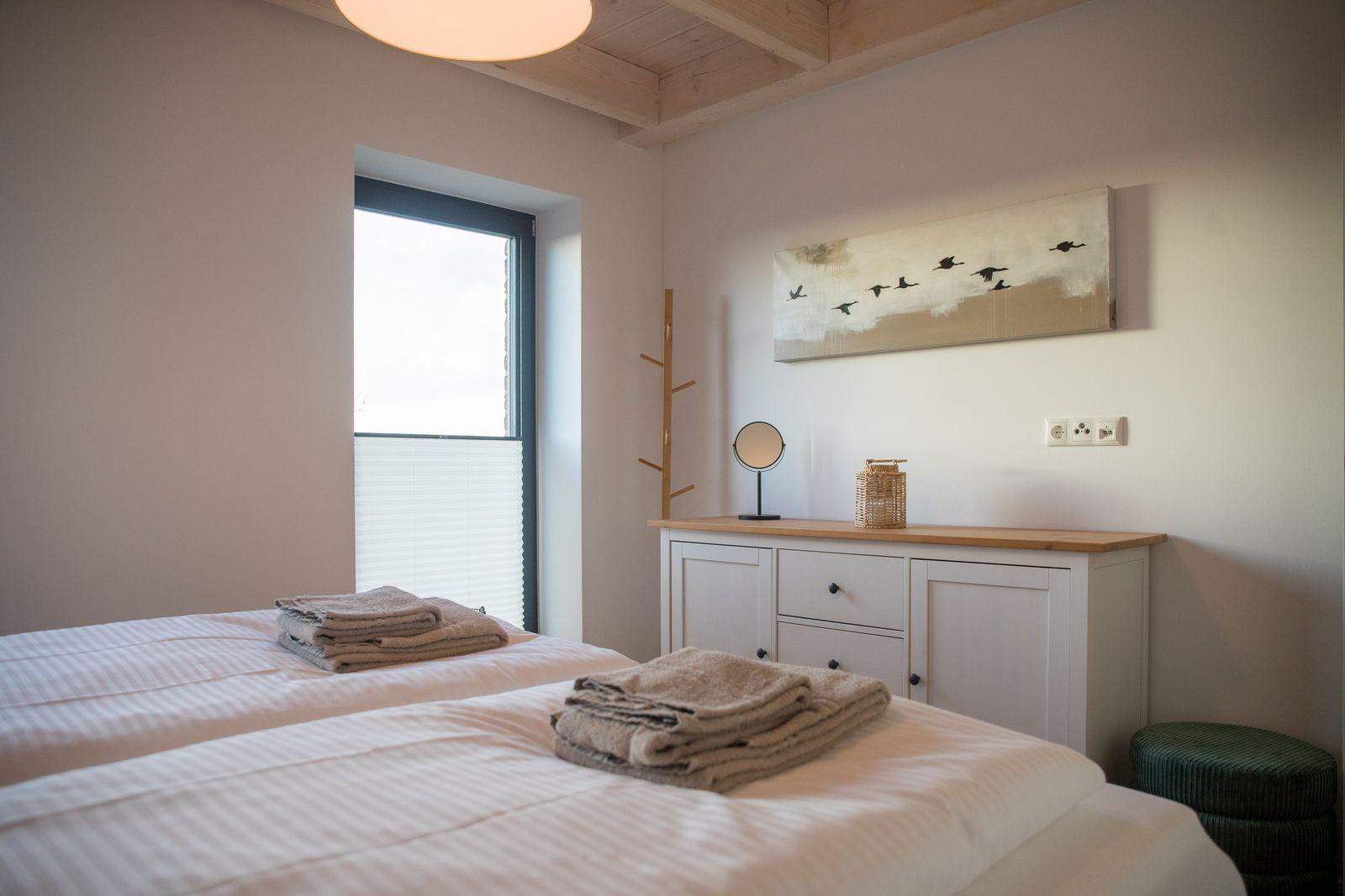 Zwei Betten mit Handtüchern, Schrank, Fenster und Wandbild.