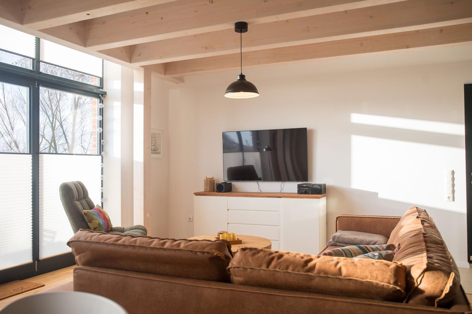 Wohnzimmer mit braunem Sofa, Fernseher und Holzbalkendecke.