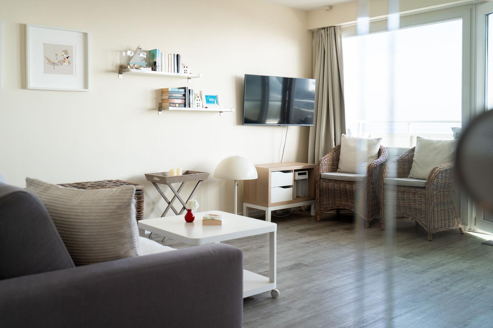 Wohnzimmer mit Sofa, Fernseher und Sitzgelegenheiten an der Glasfront.