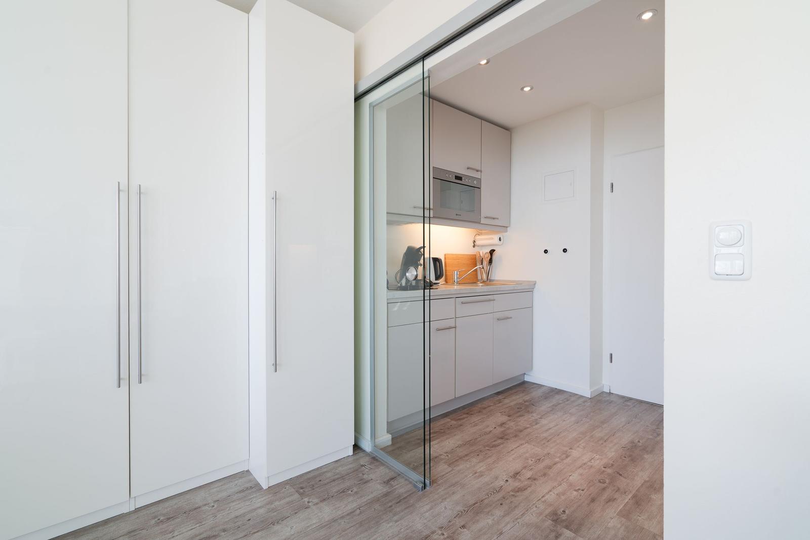 Küche mit Glaswand und weißen Schränken. Holzfußboden und integrierte Geräte.