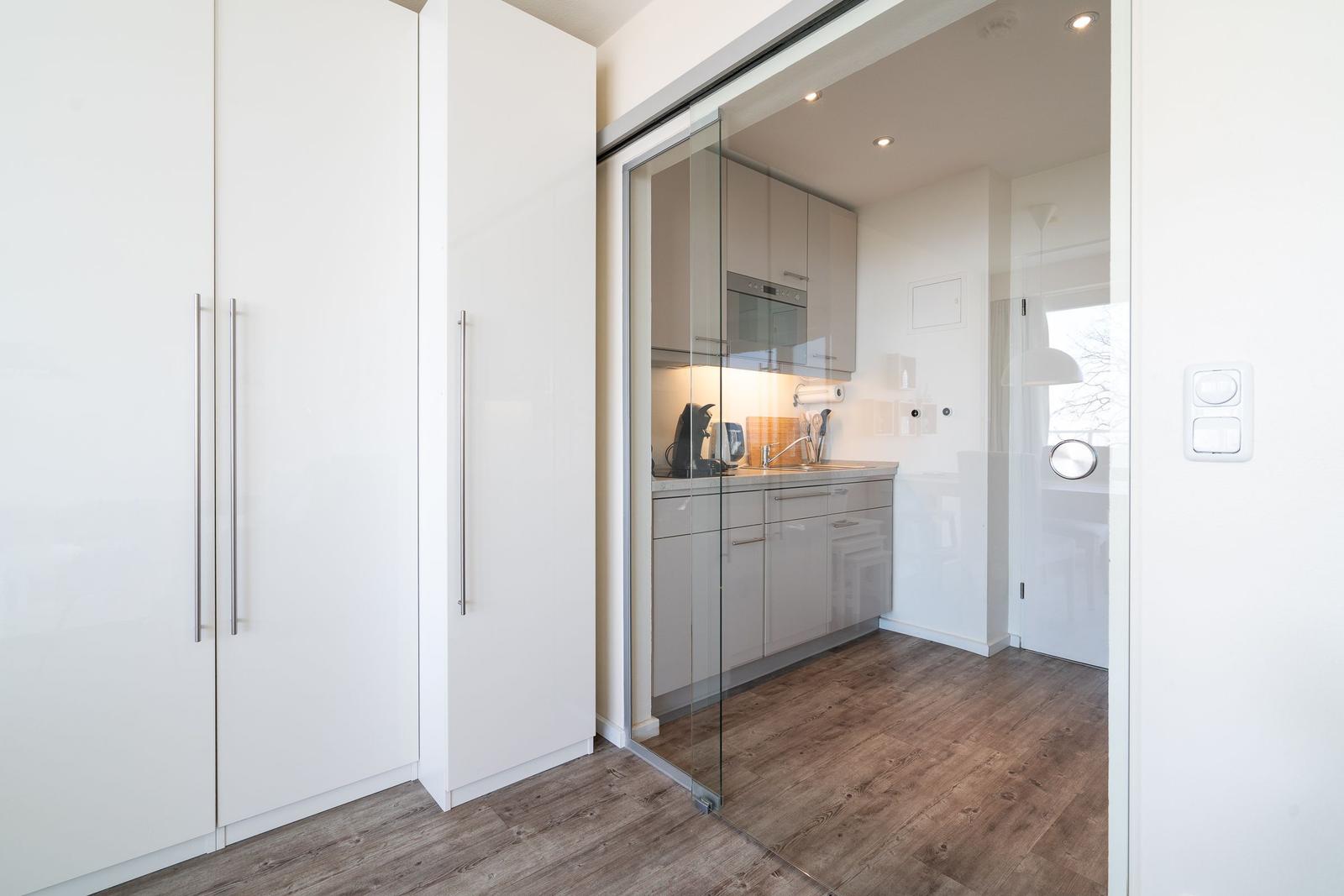 Küche mit Glaswand und weißen Schränken. Holzfußboden und moderne Einbauküche.