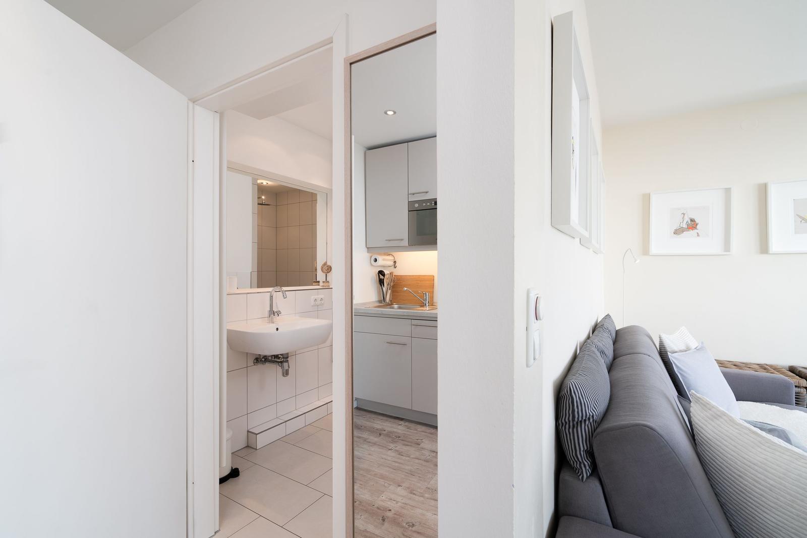 Wohnzimmer mit Sofa, Küche und Bad im Hintergrund.