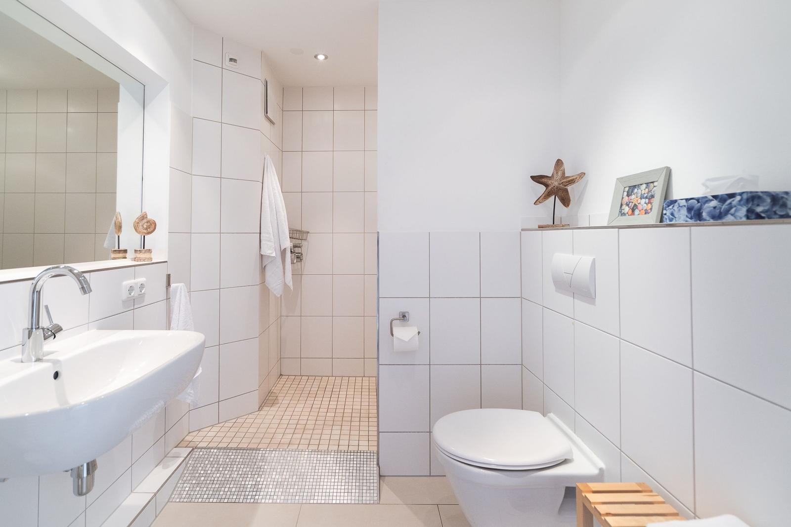 Badezimmer mit Dusche, Waschbecken und Toilette. Weiße Fliesen und dekorative Elemente.