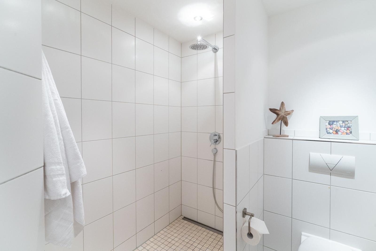 Dusche mit Duschbrause, Toilette und Handtuch an der Wand.