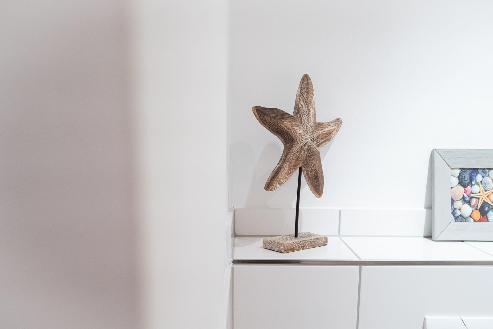 Holzstern auf Standfuß neben Bild mit Muscheln und Steinen.