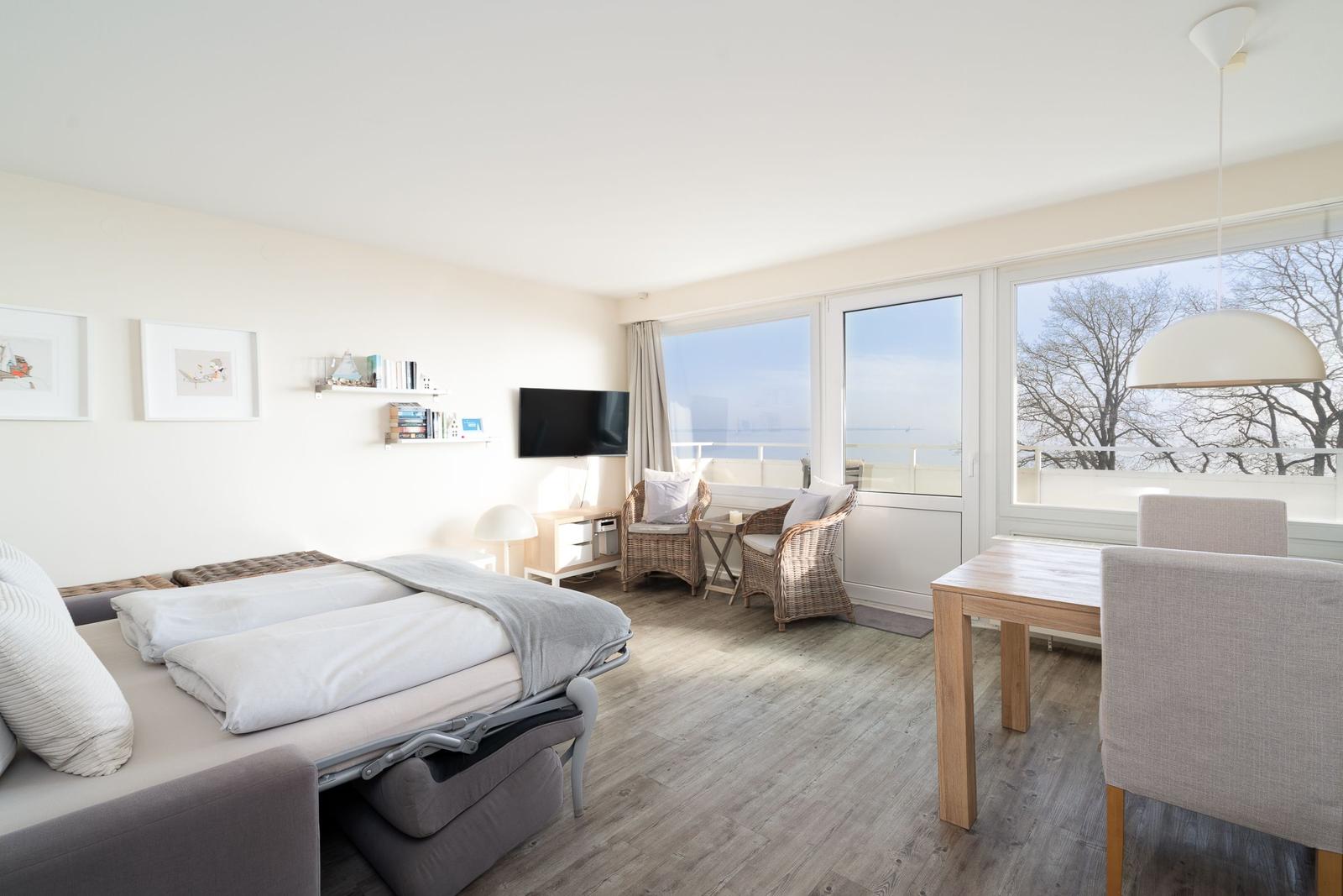 Zimmer mit Bett, TV, Esstisch und Balkon mit Blick auf Wasser.
