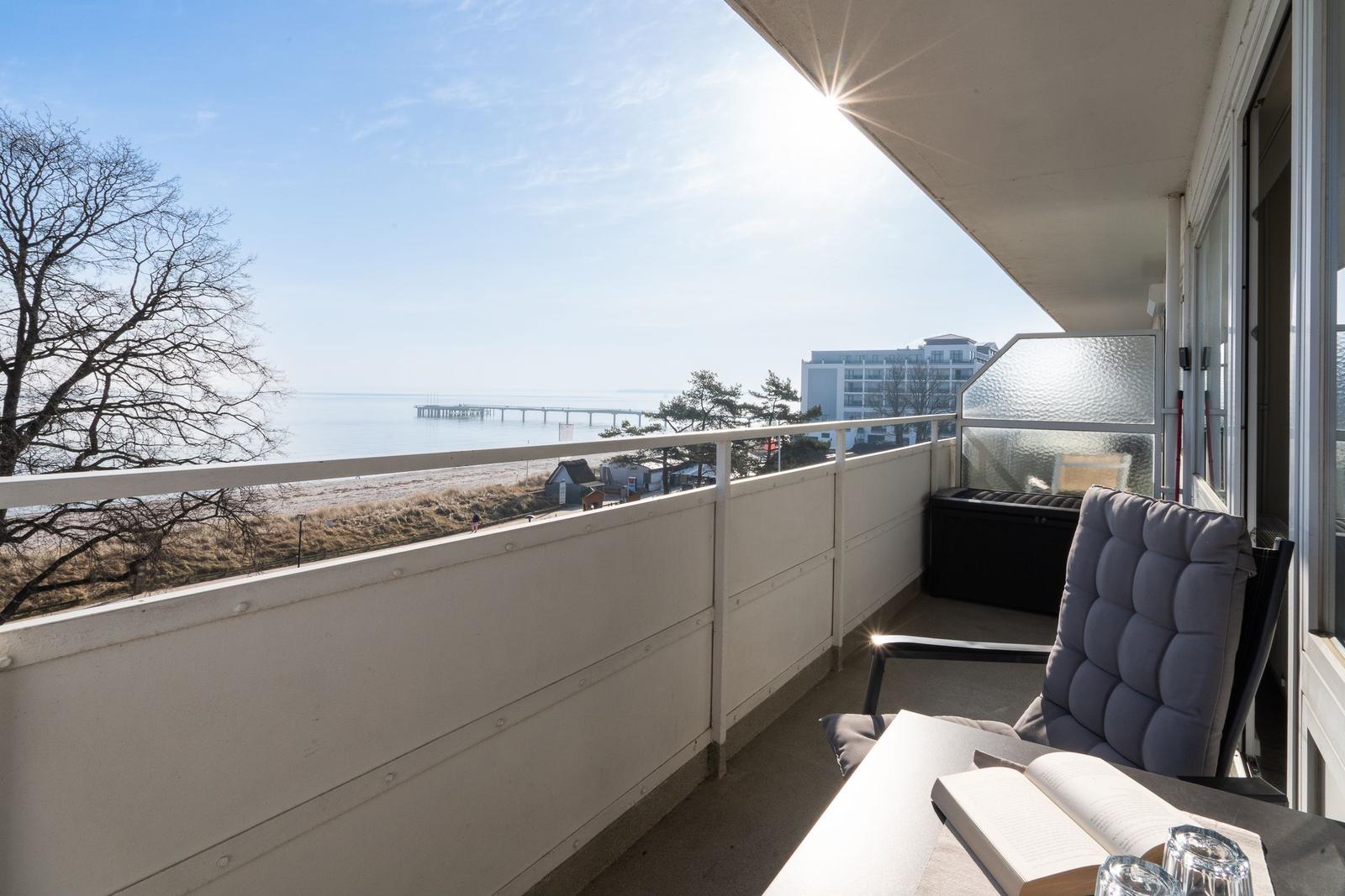 Balkon mit Sitzgelegenheit und Meerblick auf Pier und Strand.