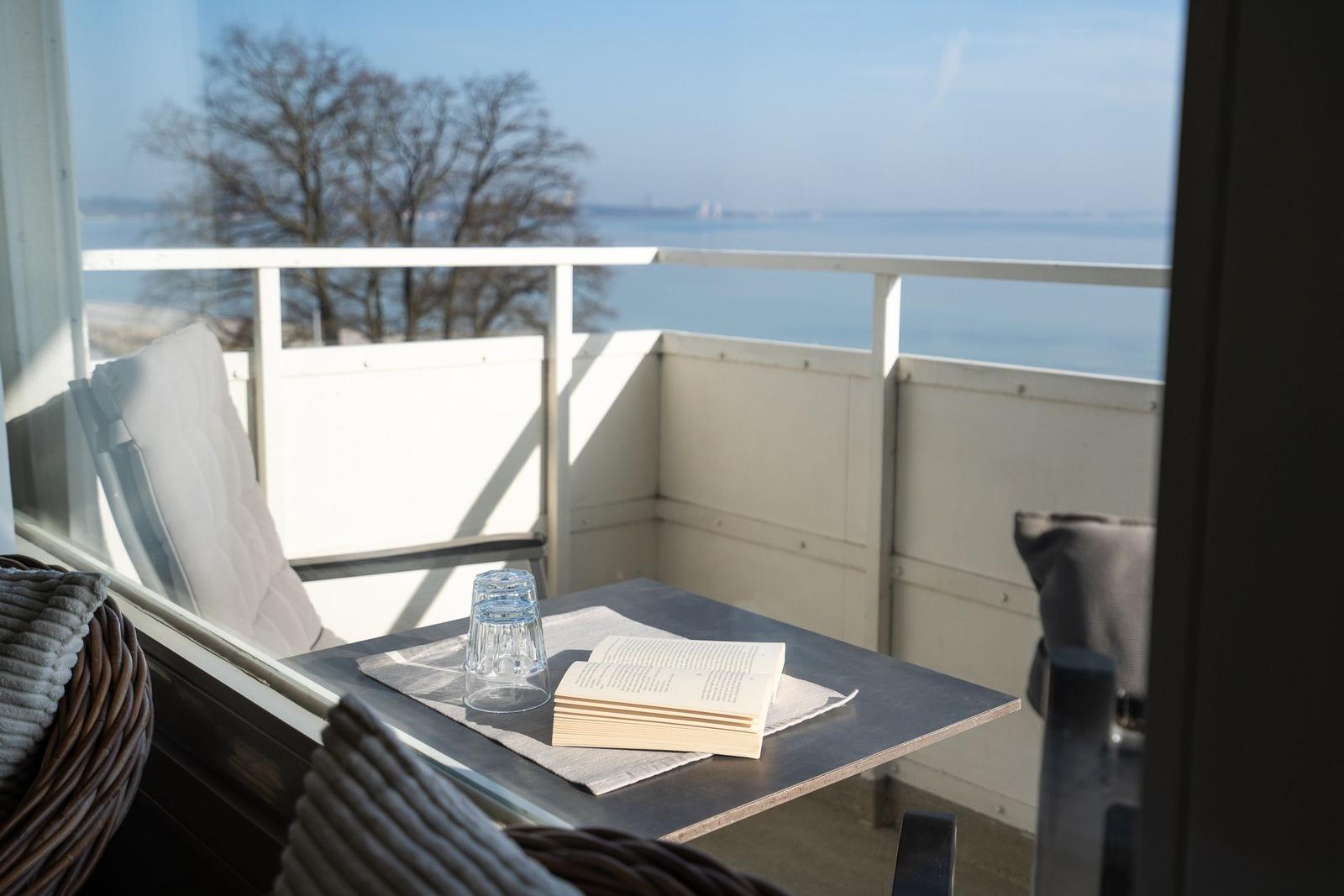 Balcony with table, book, and glasses overlooking the sea.