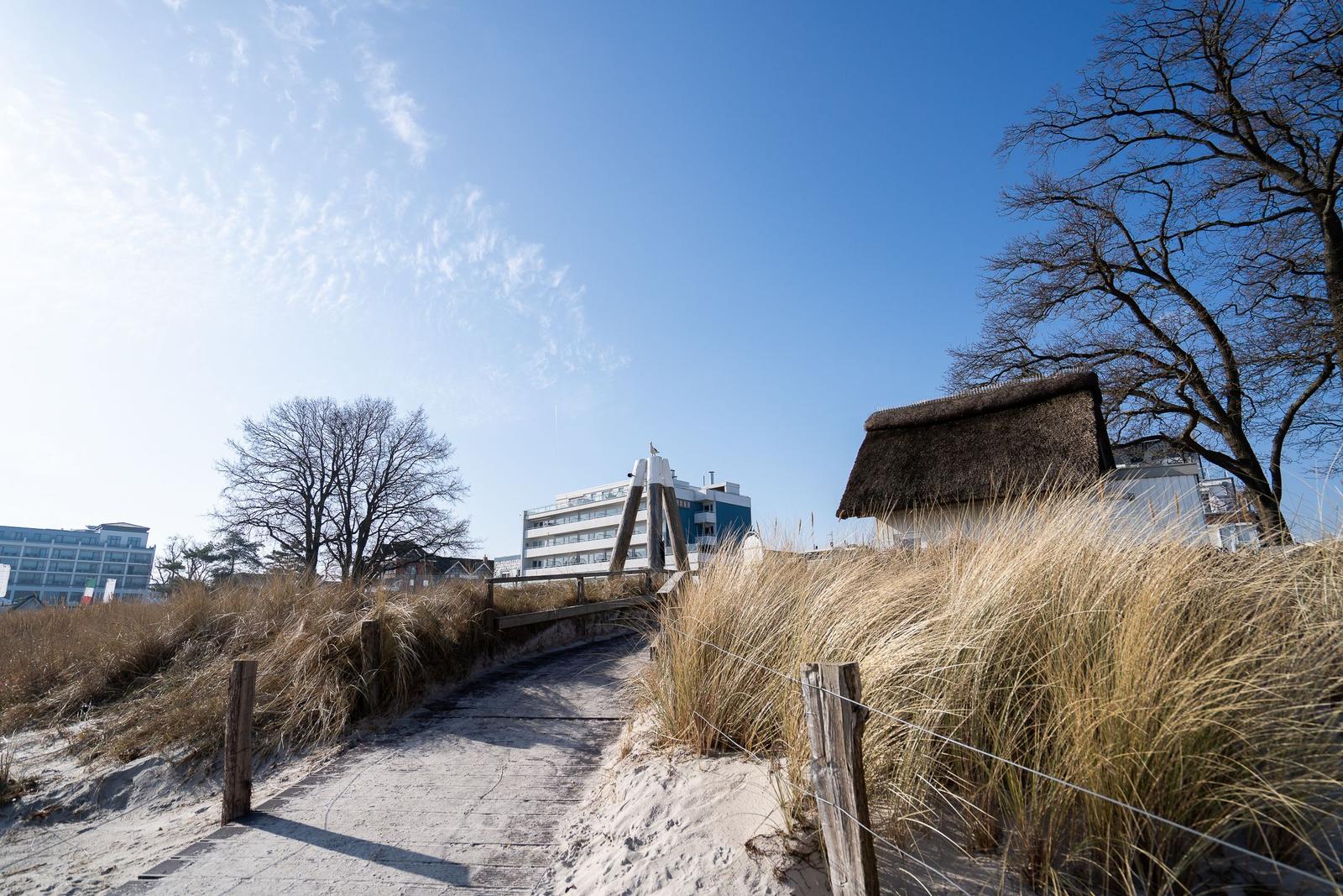 Weg durch Dünen mit Strohdachhaus und Hotels im Hintergrund.