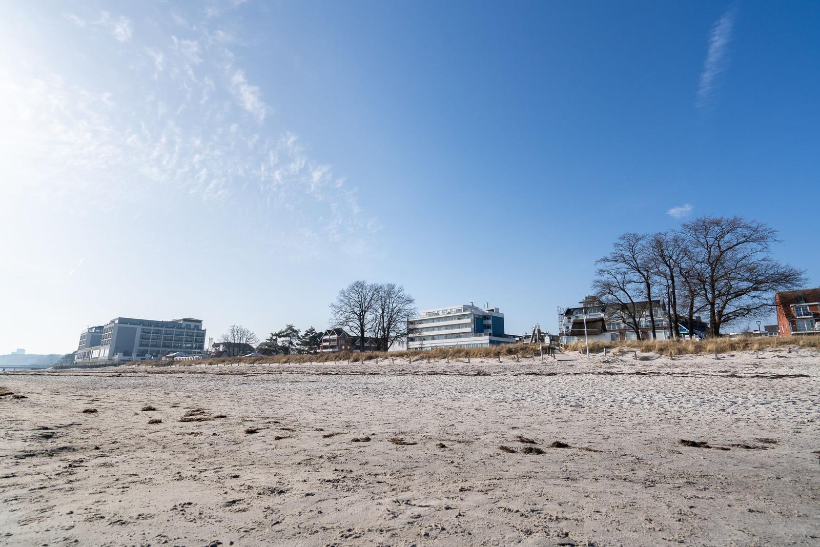 Strand mit Sand und Gebäuden im Hintergrund unter blauem Himmel.